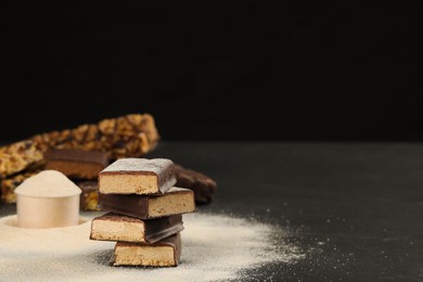 Photo of Tasty energy bars and protein powder on black table, space for text