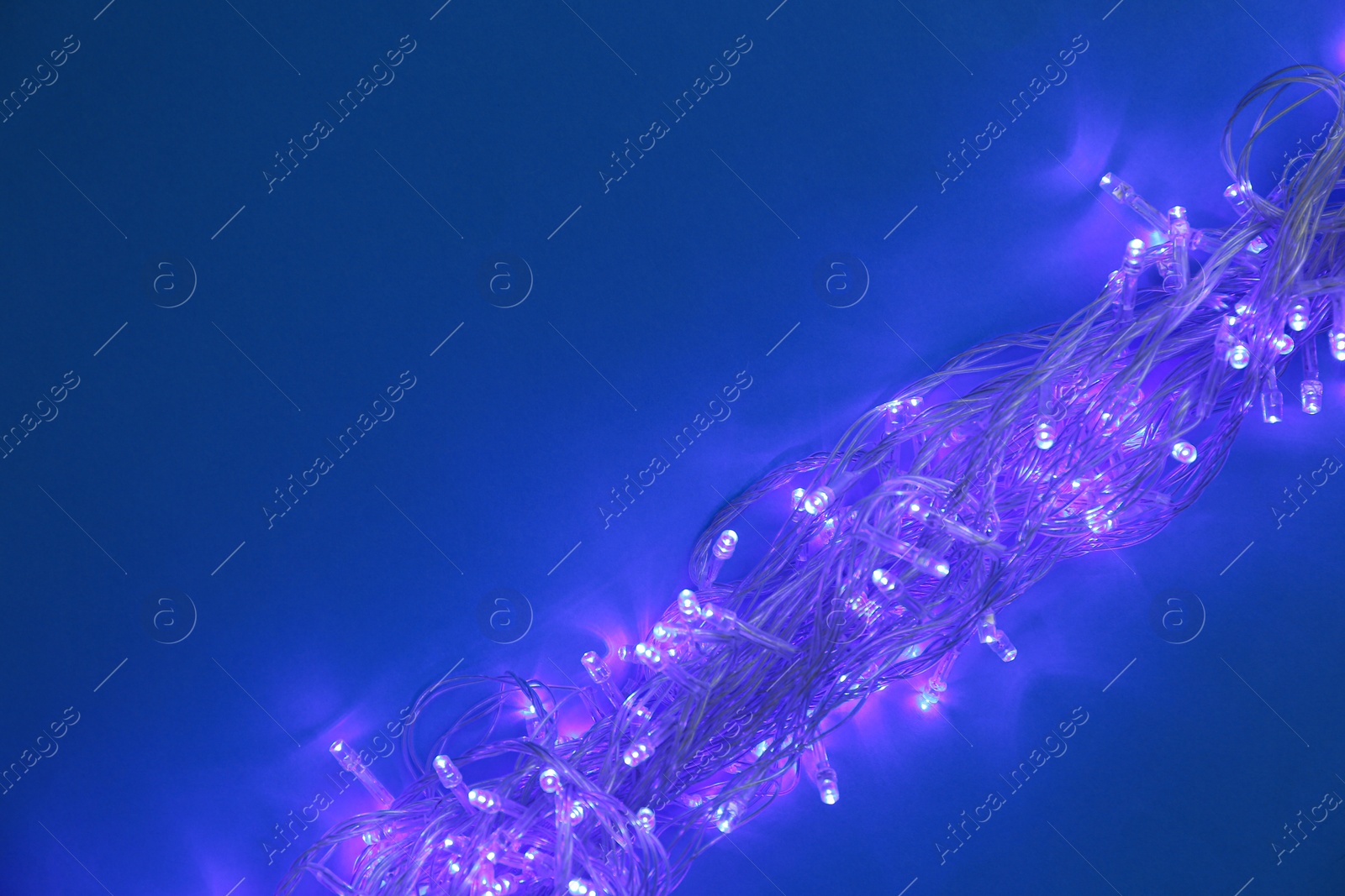 Photo of Glowing Christmas lights on dark blue background, top view. Space for text