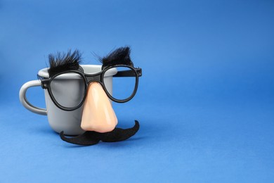 Photo of Man's face made of cup, fake mustache, nose and glasses on blue background. Space for text