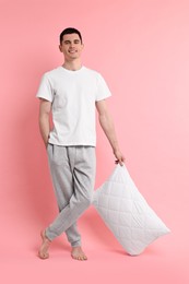 Photo of Happy man in pyjama holding pillow on pink background