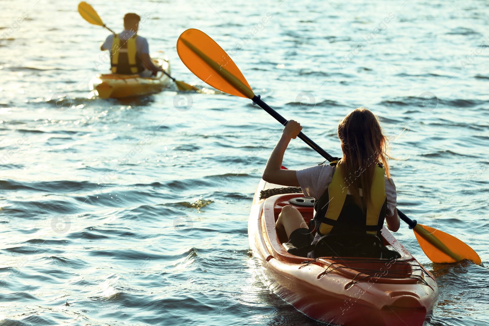 Photo of Couple in life jackets kayaking on river, back view. Summer activity