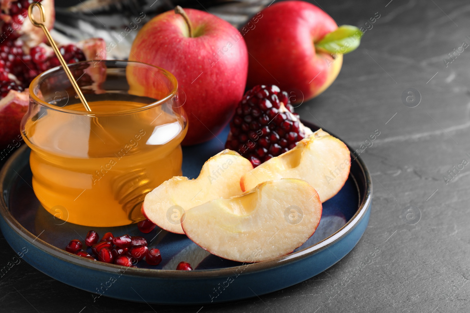 Photo of Honey, pomegranate and apples on black table, closeup. Rosh Hashana holiday