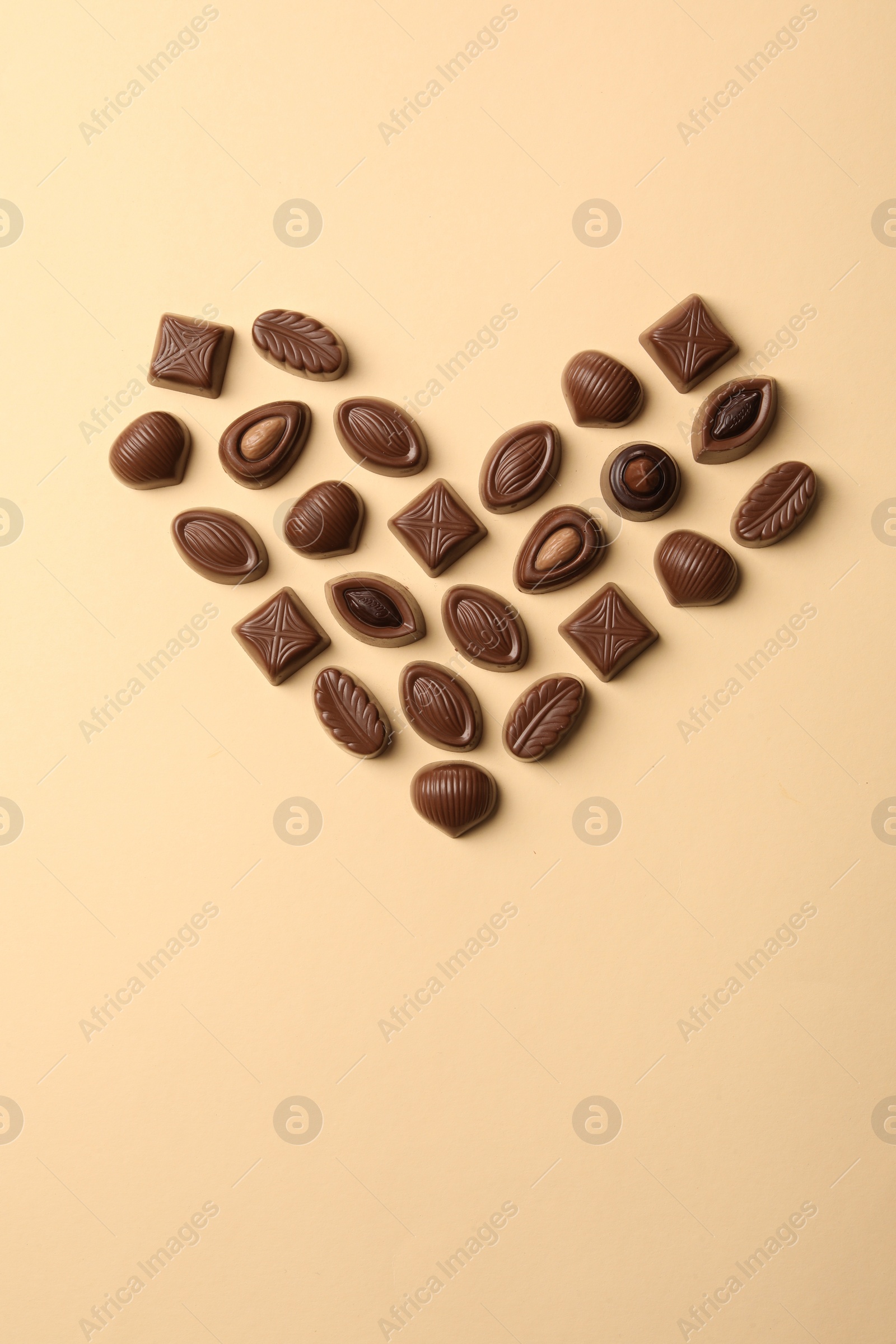 Photo of Heart made with delicious chocolate candies on beige background, top view