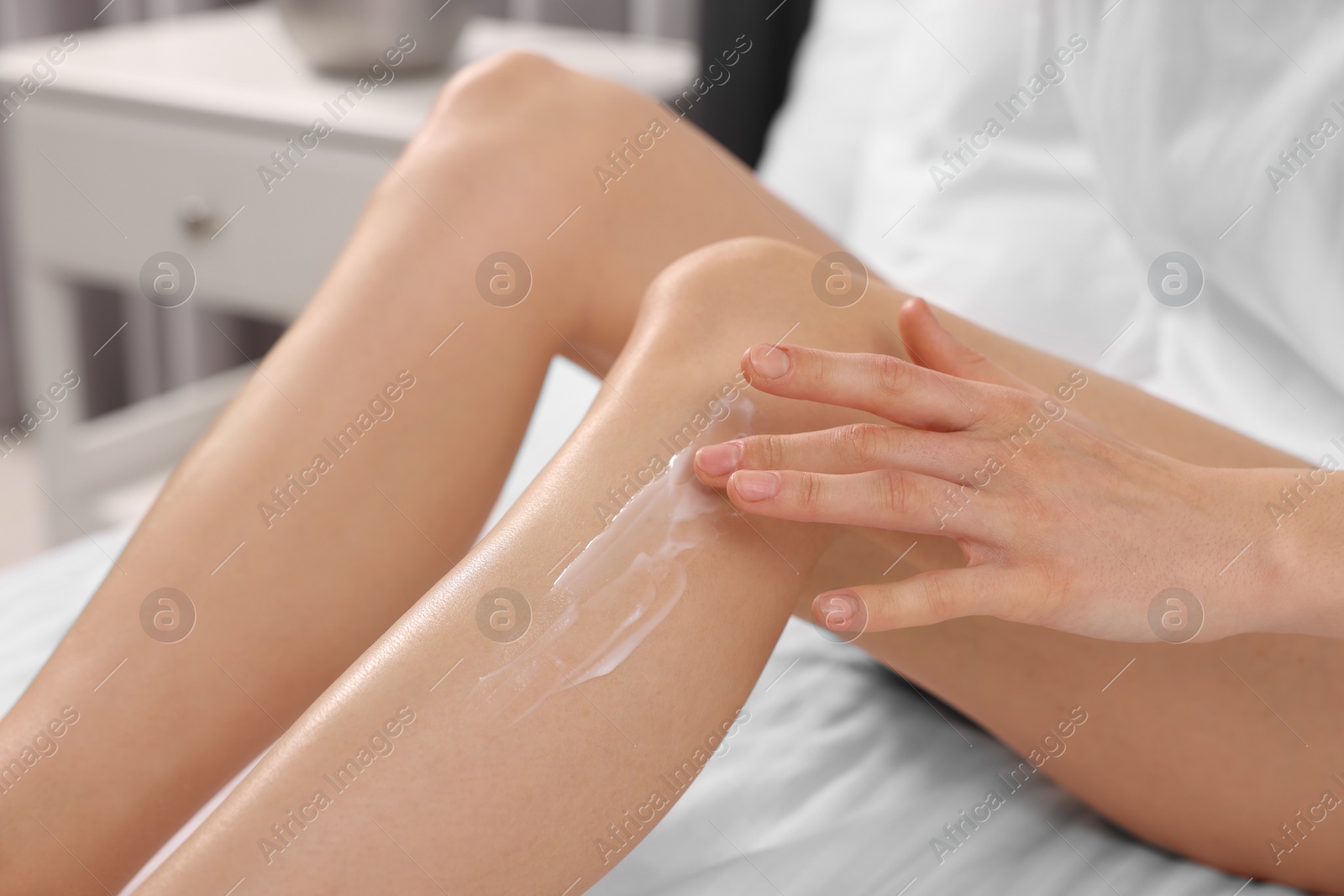 Photo of Woman applying cream onto leg in bedroom, closeup