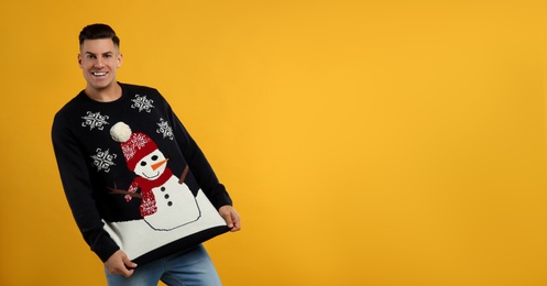 Happy man showing his Christmas sweater on yellow background