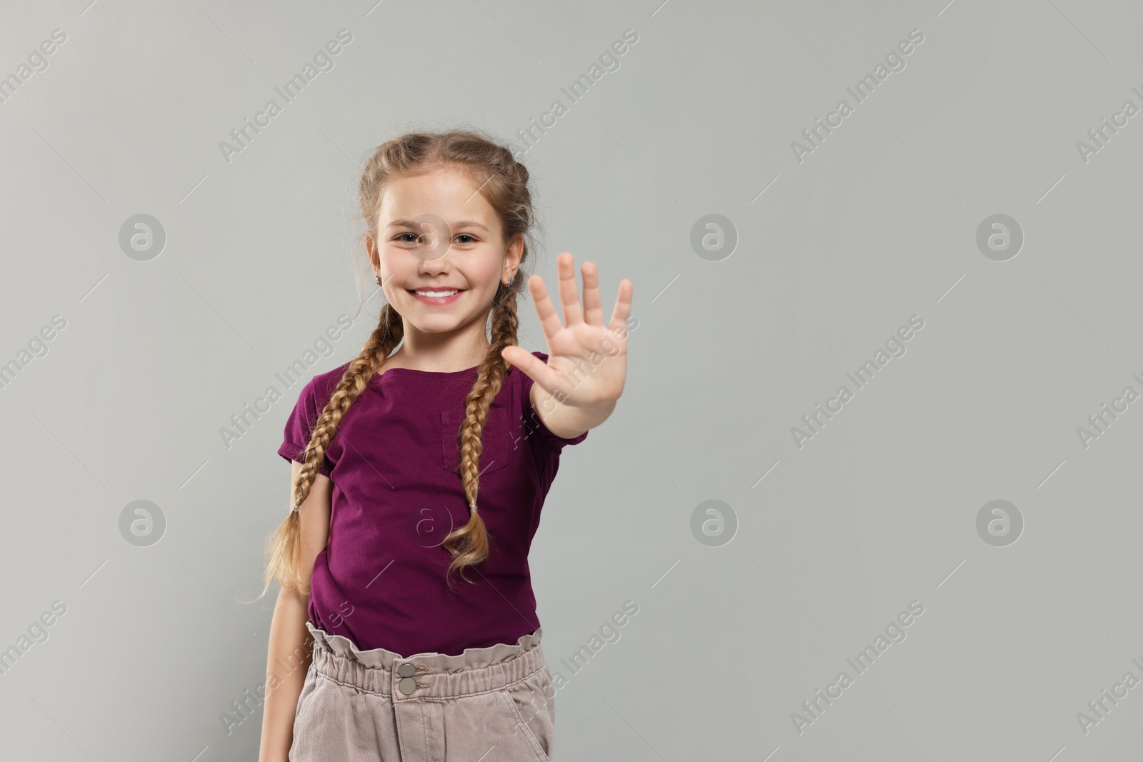 Photo of Happy girl giving high five on light grey background, space for text