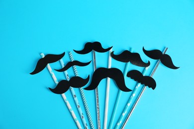 Fake paper mustaches with party props on light blue background, flat lay