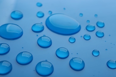 Photo of Drops of spilled water on blue background, closeup