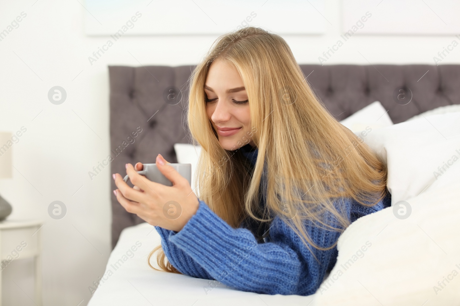 Photo of Beautiful young woman lying with cup in bed at home. Winter atmosphere