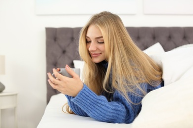 Beautiful young woman lying with cup in bed at home. Winter atmosphere