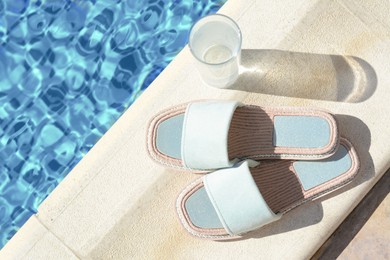 Photo of Stylish slippers and glass of water near outdoor swimming pool on sunny day, space for text