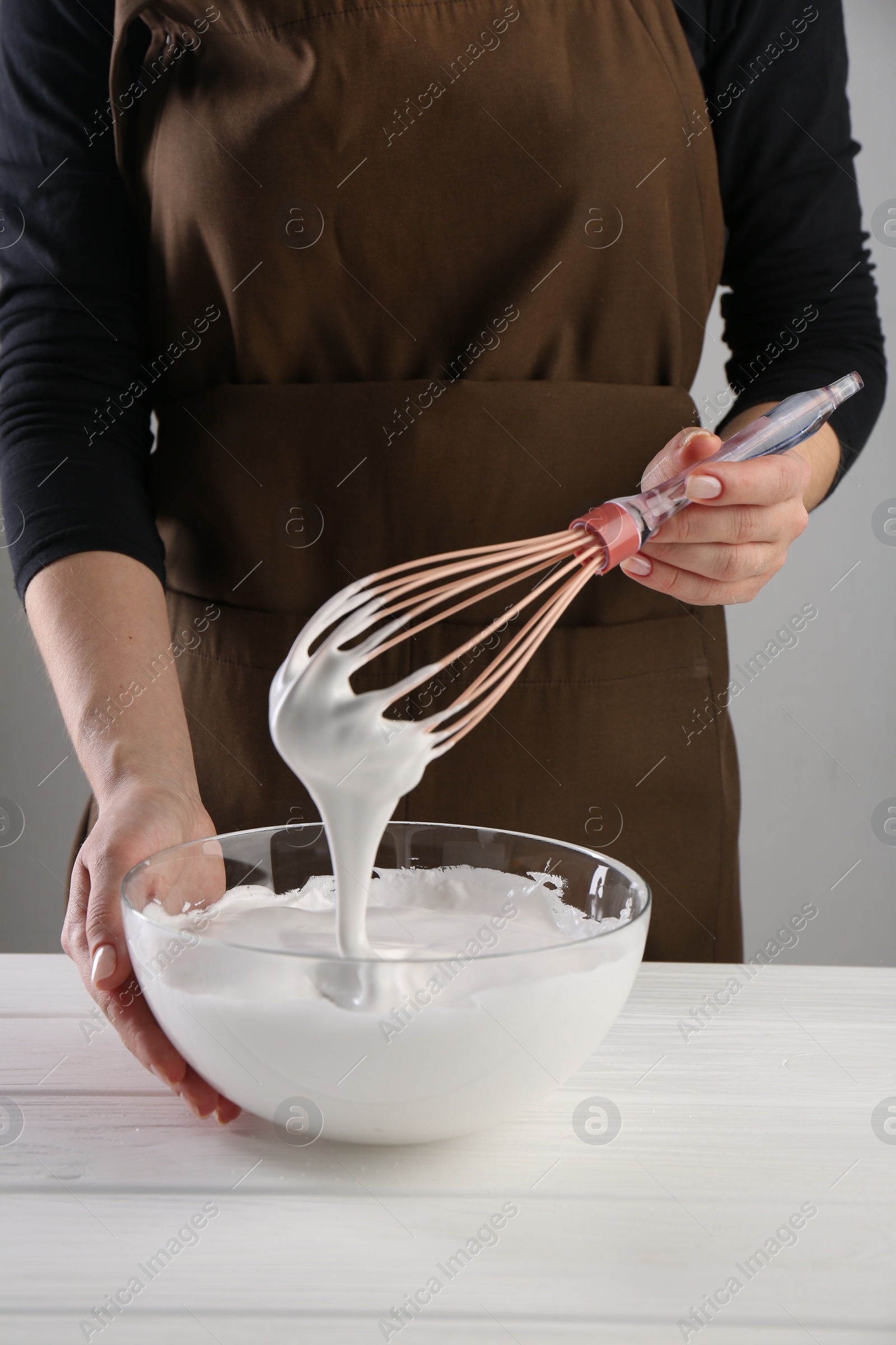 Photo of Woman making whipped cream with whisk at white wooden table, closeup