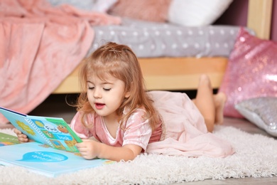 Cute little girl in princess dress reading book at home