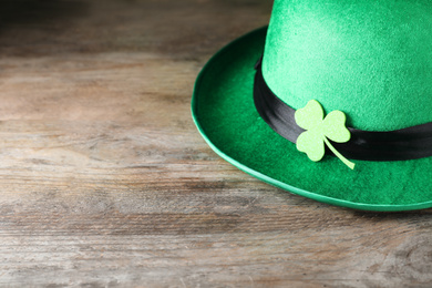 Photo of Green leprechaun hat with clover leaf on wooden table, closeup. St. Patrick's Day celebration