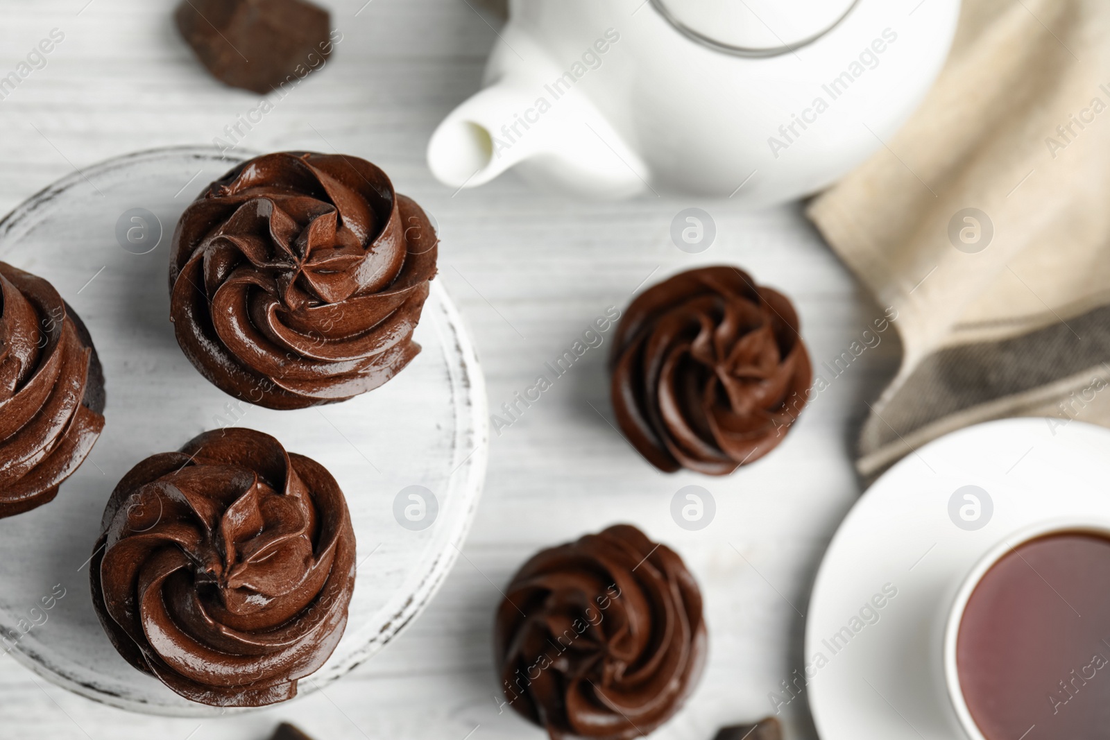 Photo of Delicious chocolate cupcakes and tea on white wooden table, flat lay