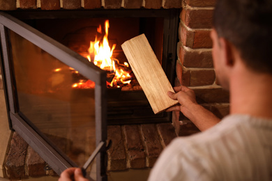 Man putting dry firewood into fireplace at home, closeup. Winter vacation