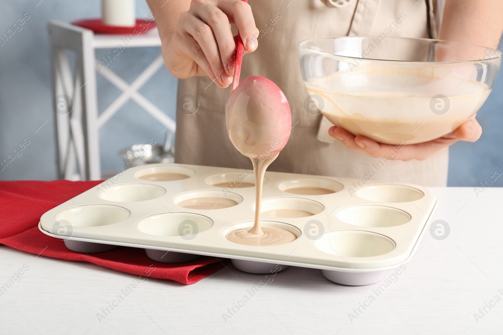 Photo of Woman pouring batter into cupcake tray at white table in kitchen, closeup