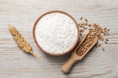 Organic flour in bowl, scoop with grains of wheat and spikelet on wooden table, flat lay