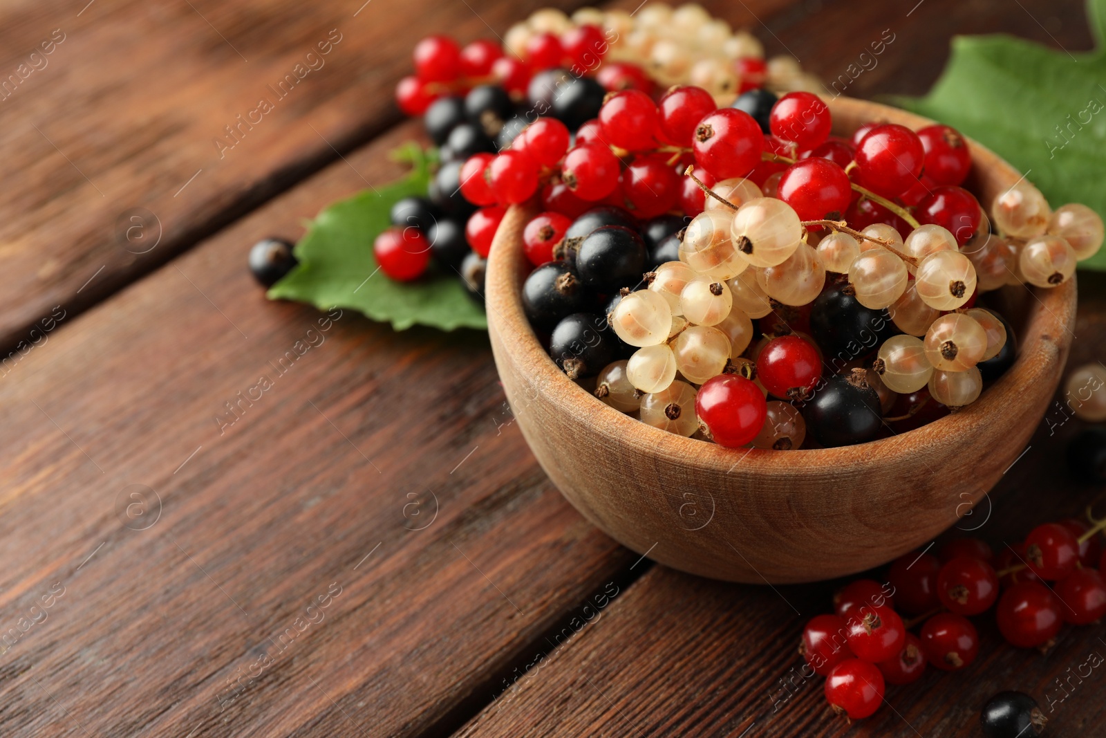 Photo of Different fresh ripe currants and green leaves on wooden table, closeup. Space for text