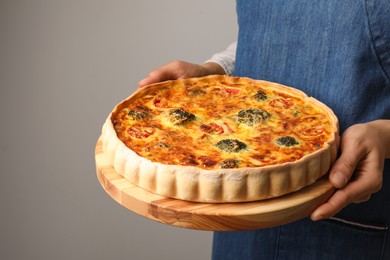 Woman holding delicious homemade vegetable quiche on light gray background, closeup