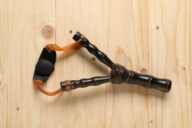 Photo of Black slingshot with pebble on wooden table, top view