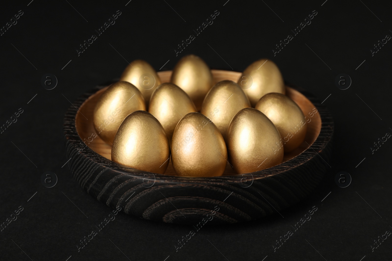 Photo of Many shiny golden eggs on black background