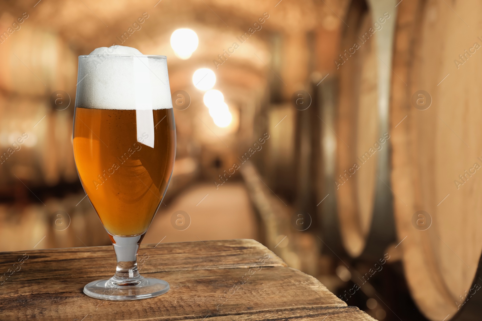 Image of Glass with fresh beer on wooden table in cellar, space for text