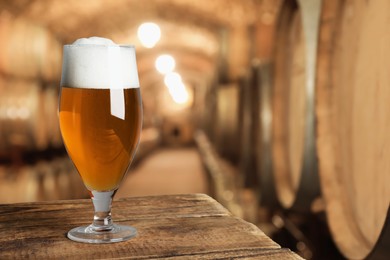 Image of Glass with fresh beer on wooden table in cellar, space for text