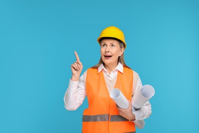 Photo of Architect in hard hat with drafts pointing at something on light blue background, space for text