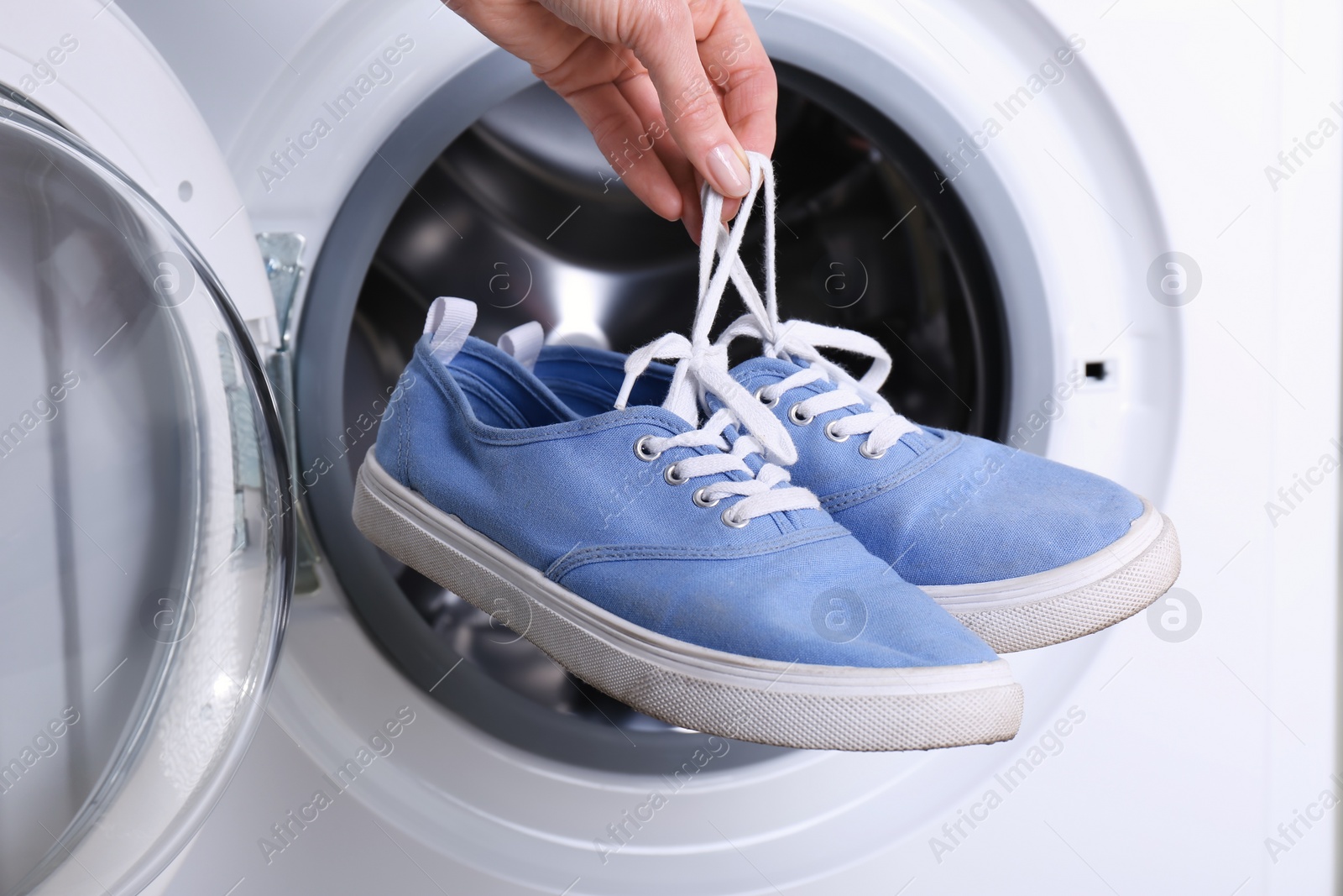 Photo of Woman putting pair of sport shoes into washing machine, closeup