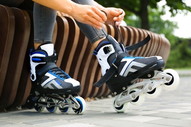 Photo of Woman wearing modern inline roller skates in city park, closeup