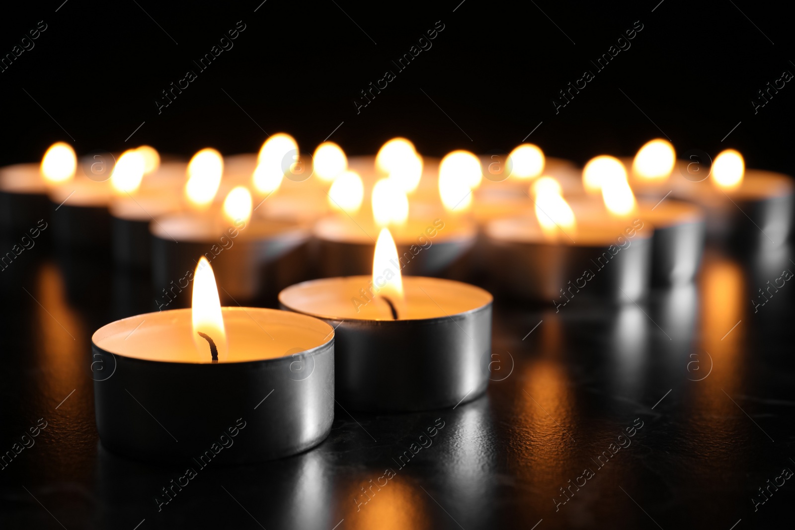 Photo of Burning candles on table in darkness, closeup. Funeral symbol