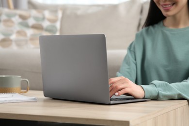 Woman working with laptop at wooden desk indoors, closeup