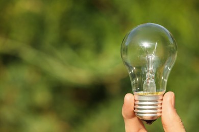Photo of Woman holding incandescent light bulb on blurred green background, closeup. Space for text