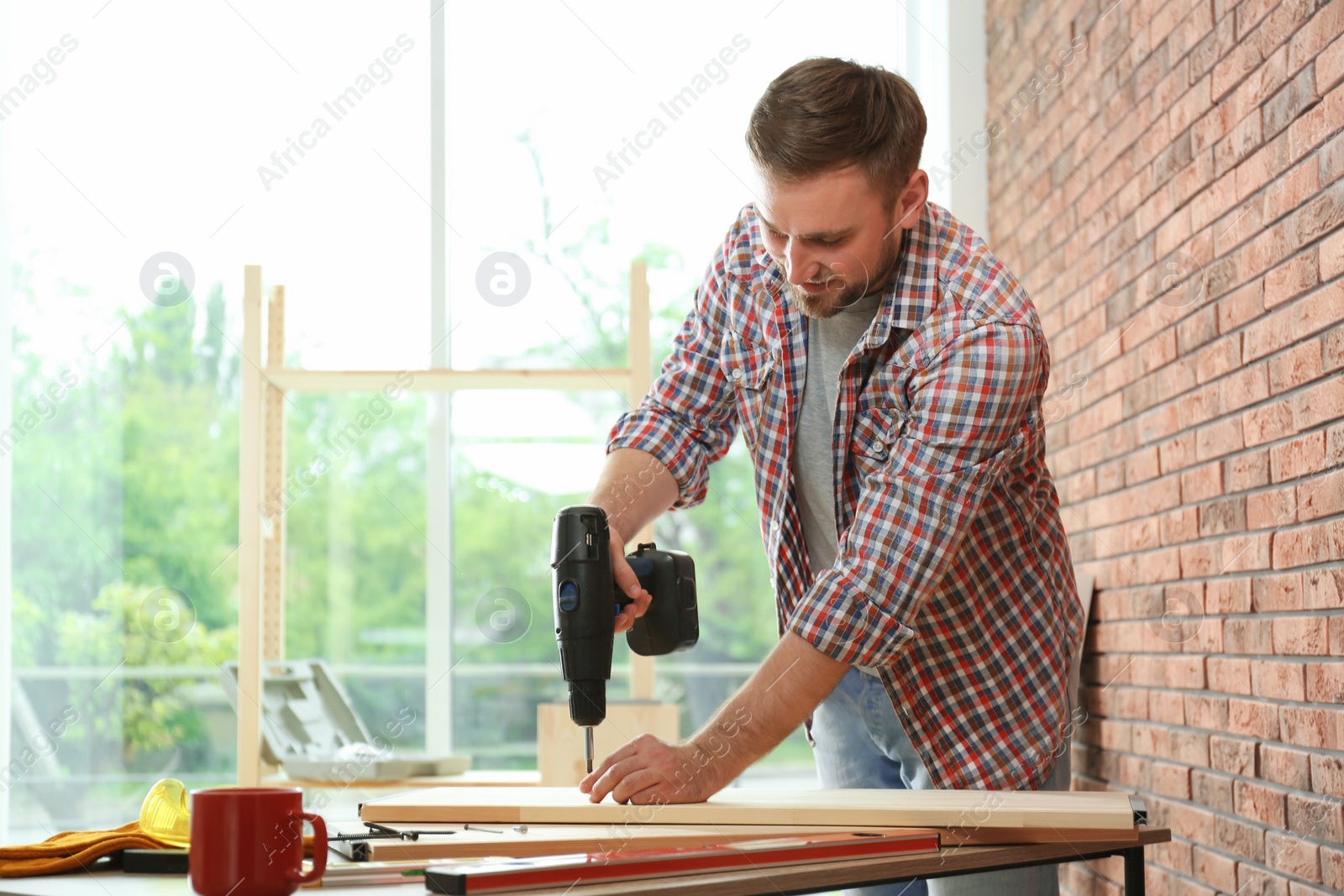 Photo of Young man working with electric screwdriver near brick wall. Space for text