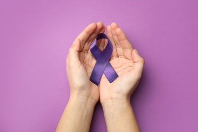 Photo of Woman holding purple ribbon on lilac background, top view. Domestic violence awareness
