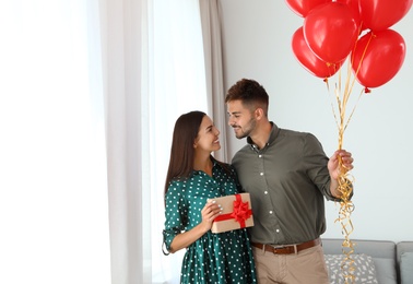 Photo of Young couple with air balloons and gift box at home. Celebration of Saint Valentine's Day