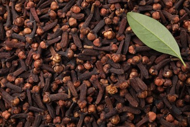 Photo of Many aromatic cloves and green leaf as background, top view. Space for text
