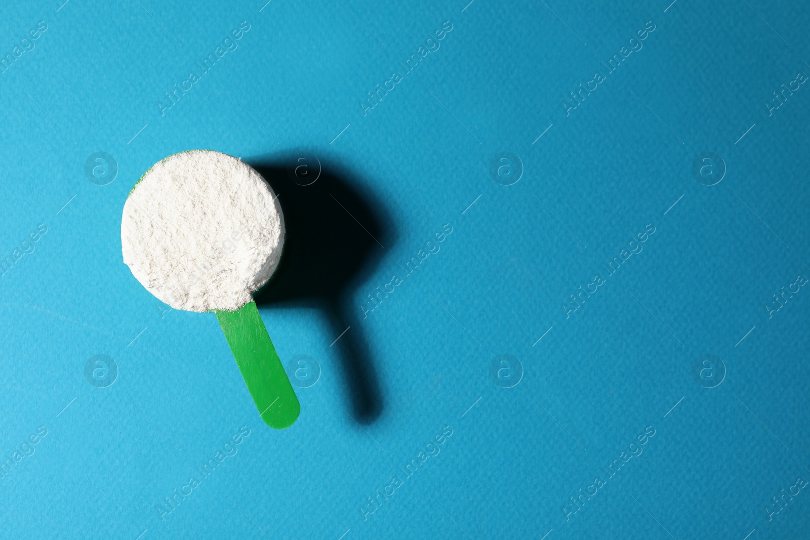 Photo of Scoop of protein powder on blue background, top view with space for text
