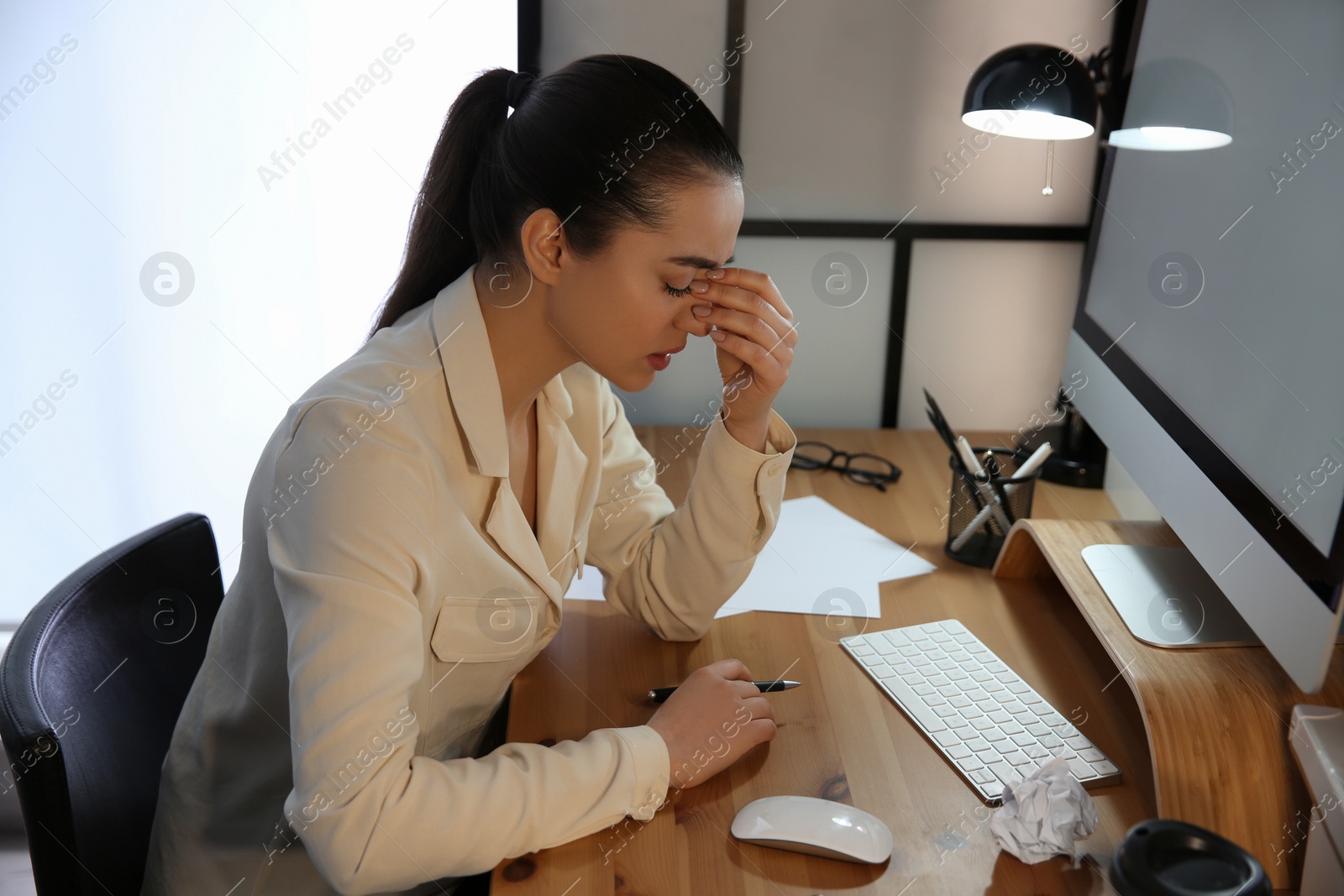 Photo of Stressed and tired young woman with headache at workplace