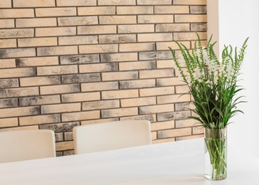 Photo of Vase with beautiful flowers on white table against brick wall. Stylish interior