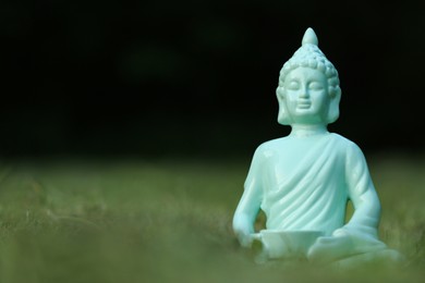 Decorative Buddha statue in green grass outdoors, space for text