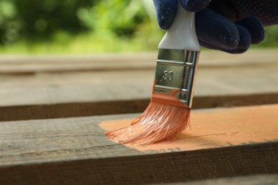 Photo of Worker painting wooden surface with coral dye outdoors, closeup. Space for text