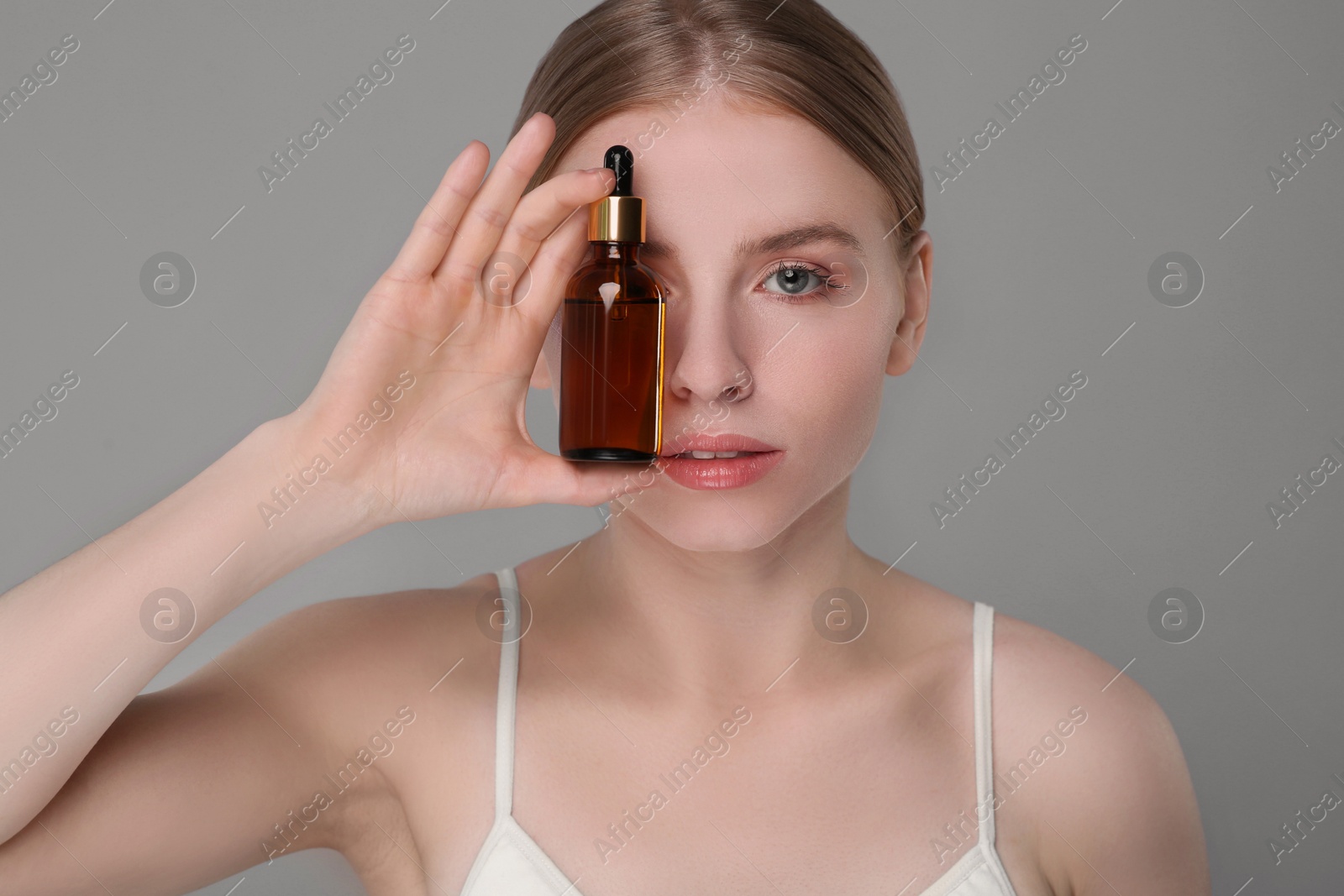 Photo of Beautiful young woman with bottle of essential oil on light grey background