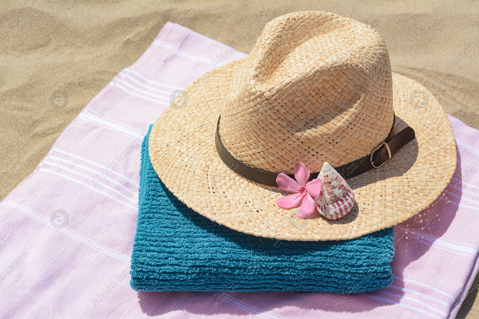 Photo of Blanket with towel, stylish straw hat and flower on sand outdoors. Beach accessories