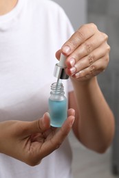 Woman with bottle of cosmetic serum and dropper on grey background, closeup
