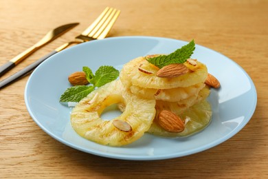 Photo of Tasty grilled pineapple slices, almonds and mint on wooden table, closeup