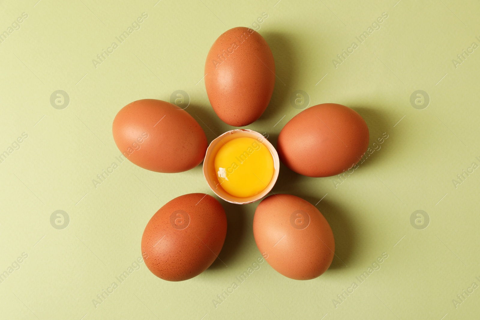 Photo of Flower made with cracked and whole chicken eggs on olive background, flat lay