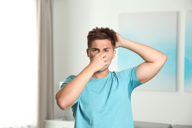 Photo of Young man with sweat stain on his clothes indoors. Using deodorant