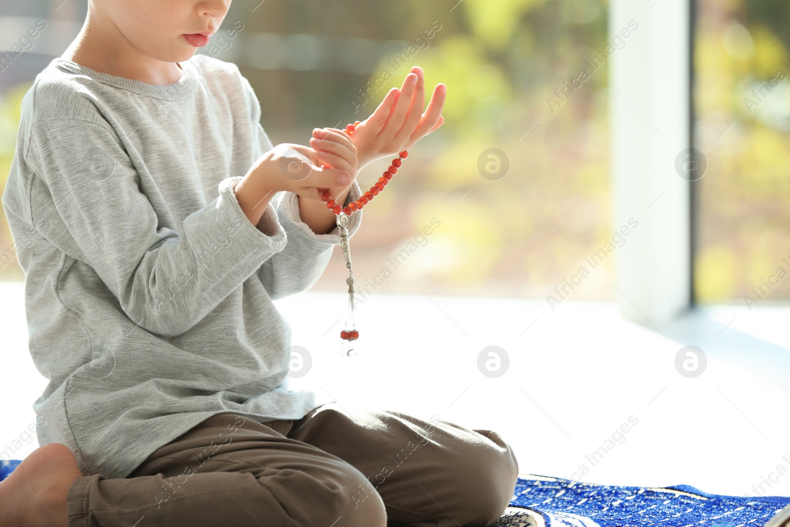 Photo of Little Muslim boy with misbaha praying on rug indoors, closeup. Space for text